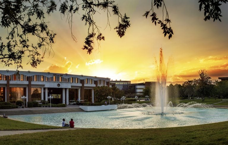 side angle photo of millican hall and the reflecting pond at sunset with the sky vibrant yellow and oranges