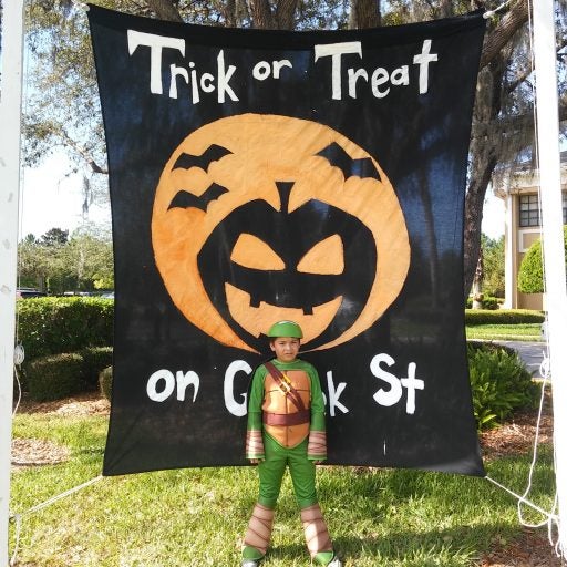 little kid dressed up as ninja turtle standing in front of trick or treat sign