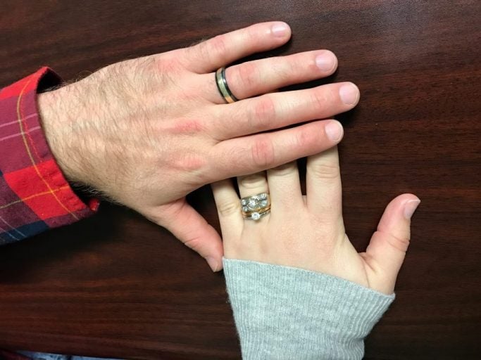 mans hand overlapping womans hand both with wedding rings