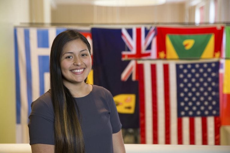 angie torres smiling in front of flags from around the world