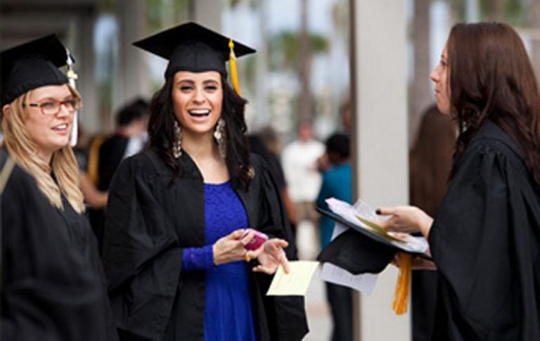 female ucf graduates smiling and talking at graduation wearing their caps and gowns