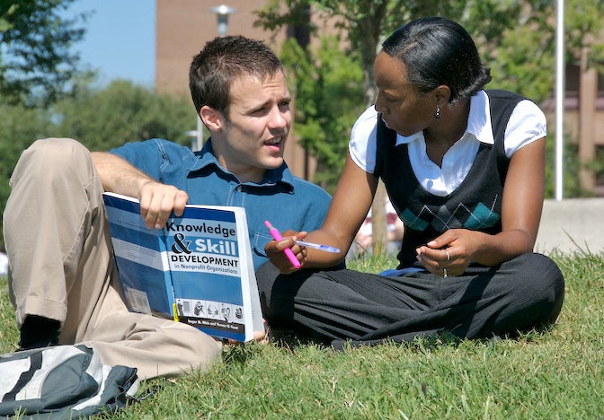 ucf male and female students sitting in grass studying with book