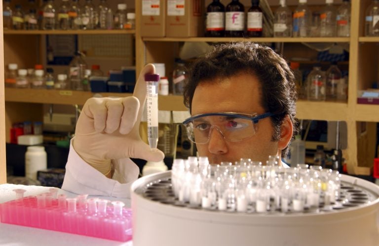 man with goggles in lab looking closely at test tube