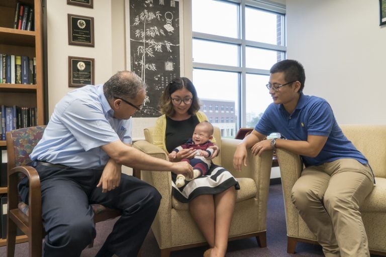 Engineering Graduate Students sitting in chairs, the woman holding a baby