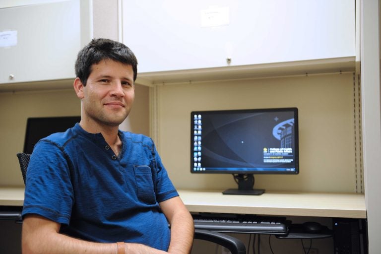 man in blue scrubs sitting a desk with computer monitor on