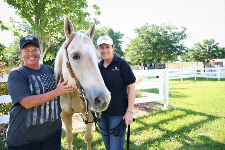 Kelly and Monroe standing on either side of a white horse