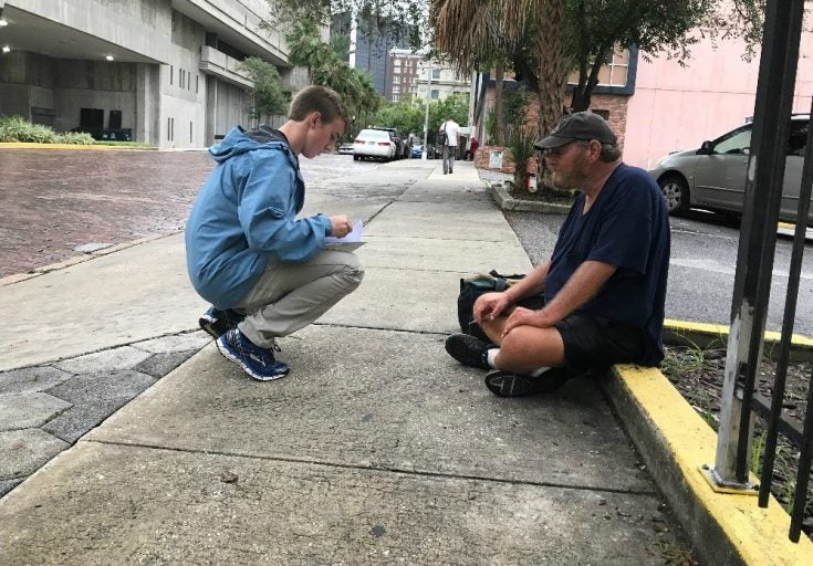 student kneeling talking to homeless man, warning him about hurricane