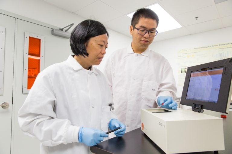 male and female in white lab coats and blue latex gloves, working on zika test