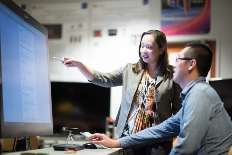 woman pointing at computer while talking about online risks for teens. man watches and listens.