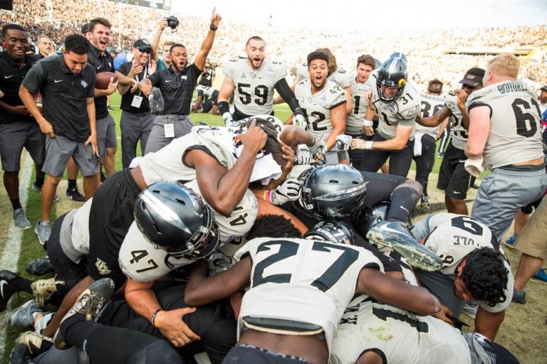 ucf knights football team celebrating victory by dog piling on the field as spectators watch