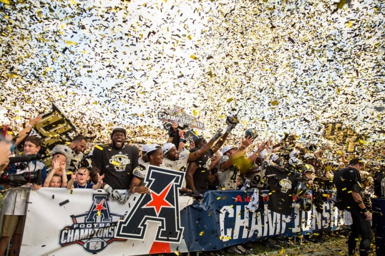 ucf football celebration with black, white, gold confetti falling from sky. banners held up.