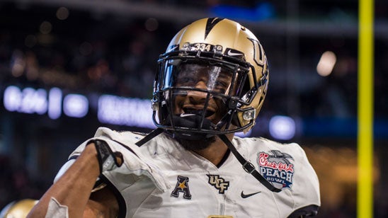 A close-up of football player wearing a white jersey is seen smiling behind his gold helmet.