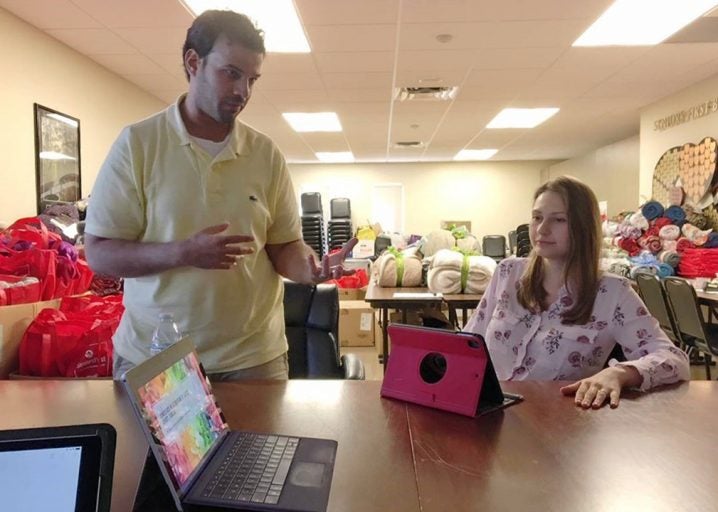 male student standing with female student sitting at desk with laptop