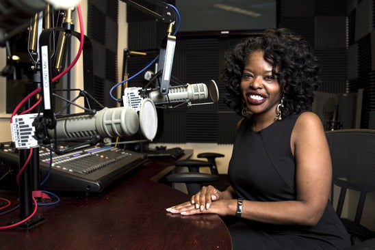 Patricia Hartley in black dress sites in front of a microphone at the Black and Gold Studios on UCF's campus.