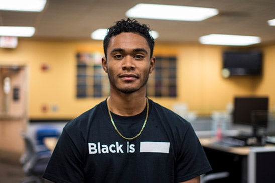 Travis Slocum wearing a black shirt with white text that reads Black Is ___.