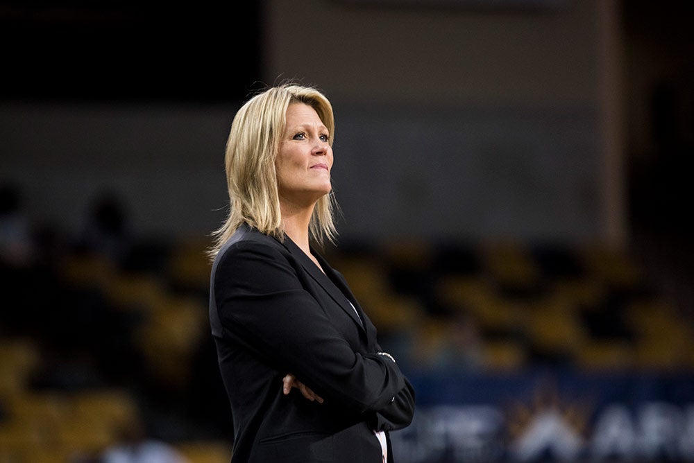 A woman with blonde hair stands with her arms crossed while wearing a black jacket.