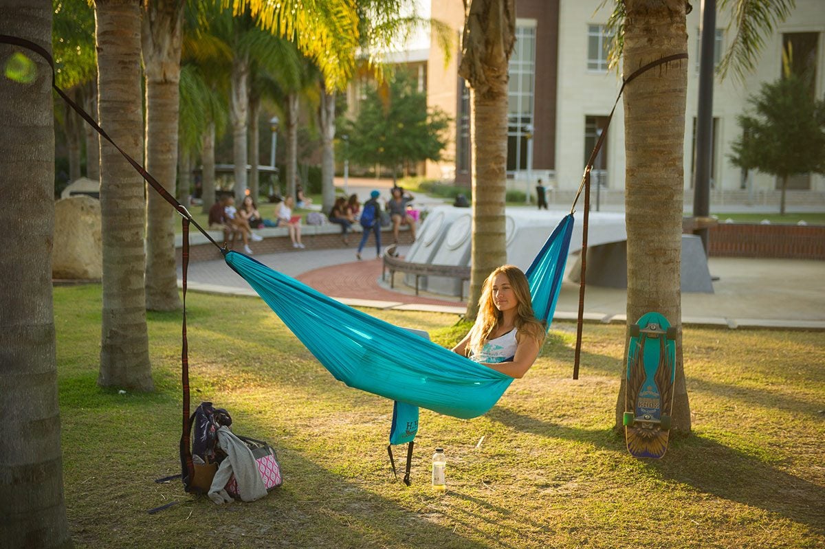 A white woman lays in a torquise hammock strung between two palm trees