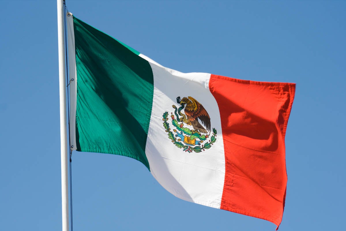 mexican flag on a flagpole waving in the wind with a blue sky in the background