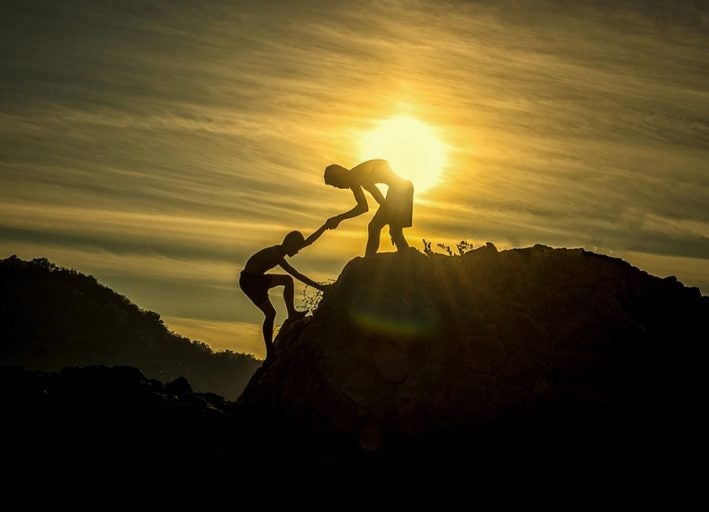 Boy giving a helping hand to another climbing a moutain.