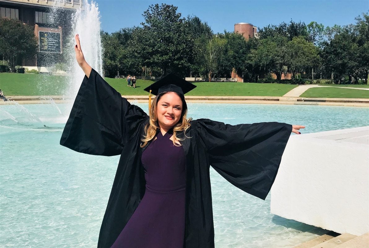 raquel in graduation cap and gown posing in front of reflecting pond
