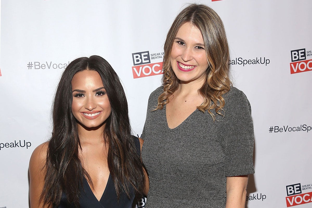 Tall, blonde woman in gray shirt poses for a photo with actress and singer Demi Lovato