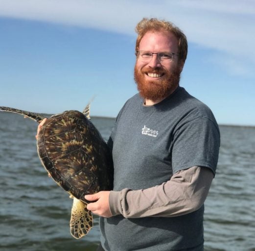ucf student Chris Long holding sea turtle while smiling on boat
