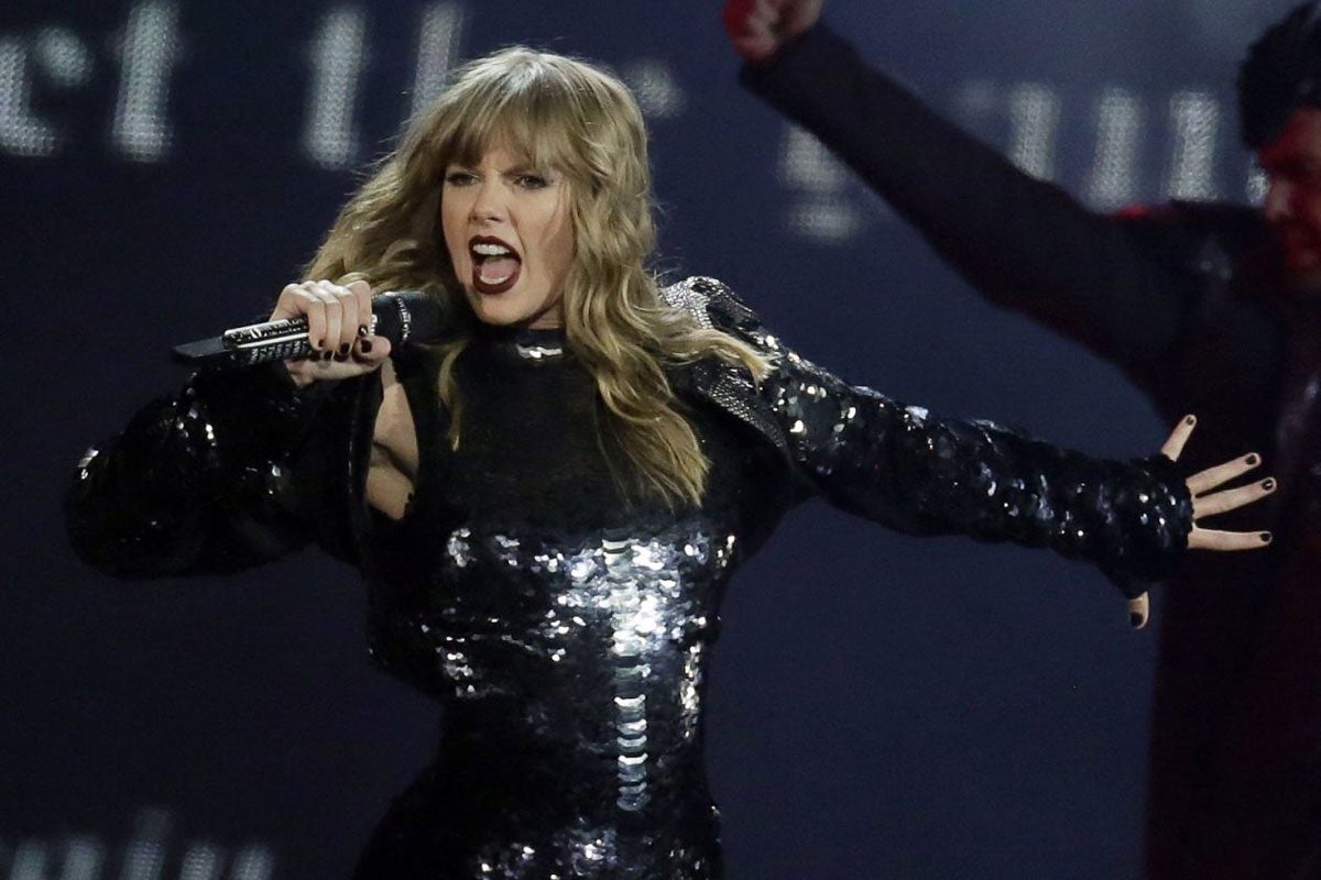 taylor swift singing into a microphone while wearing a black long sleeve body suit
