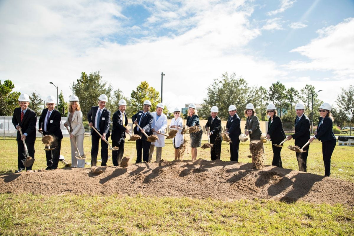 More than a dozen people lined up with shovels and picking up dirt on a partly cloudy, sunny day