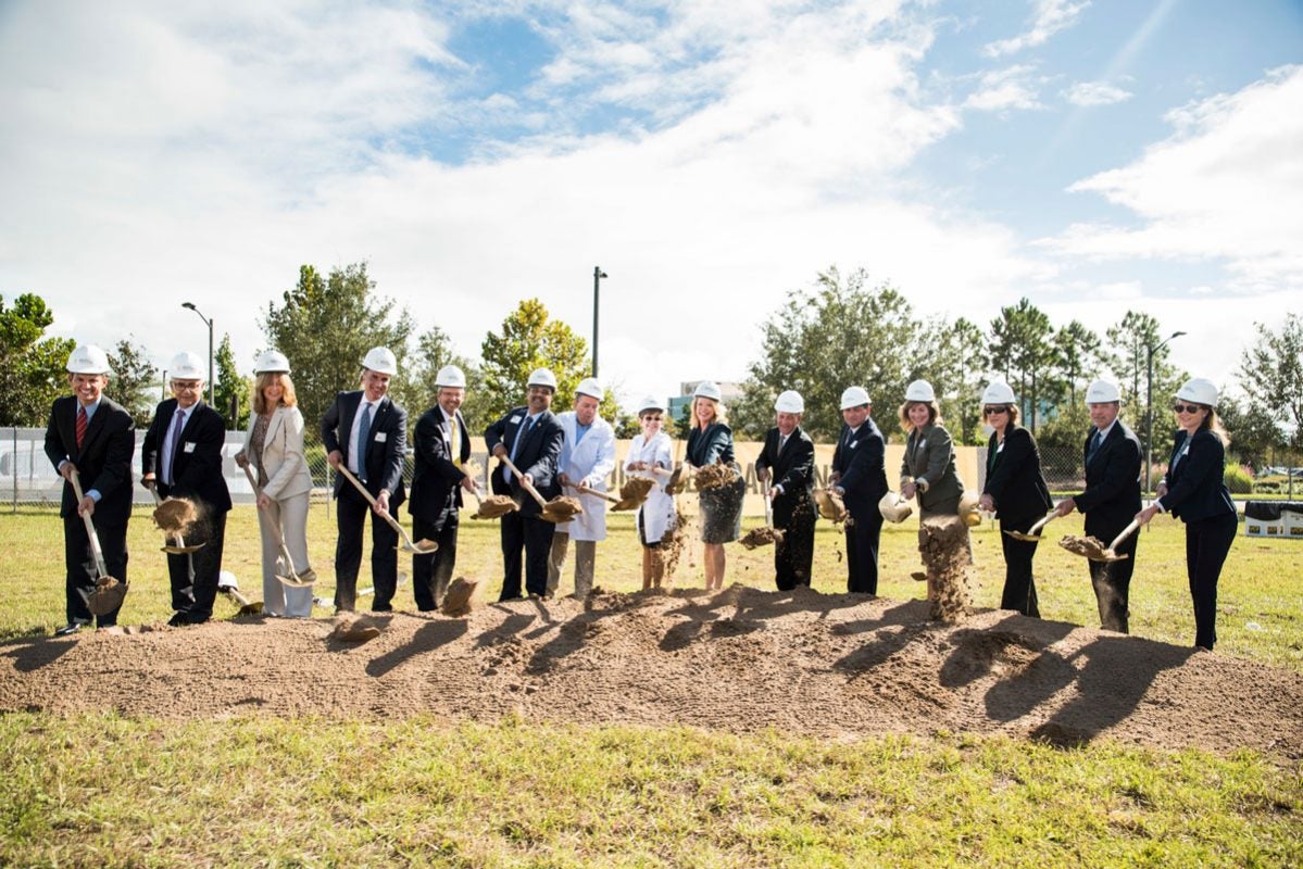 More than a dozen people lined up with shovels and picking up dirt on a partly cloudy, sunny day