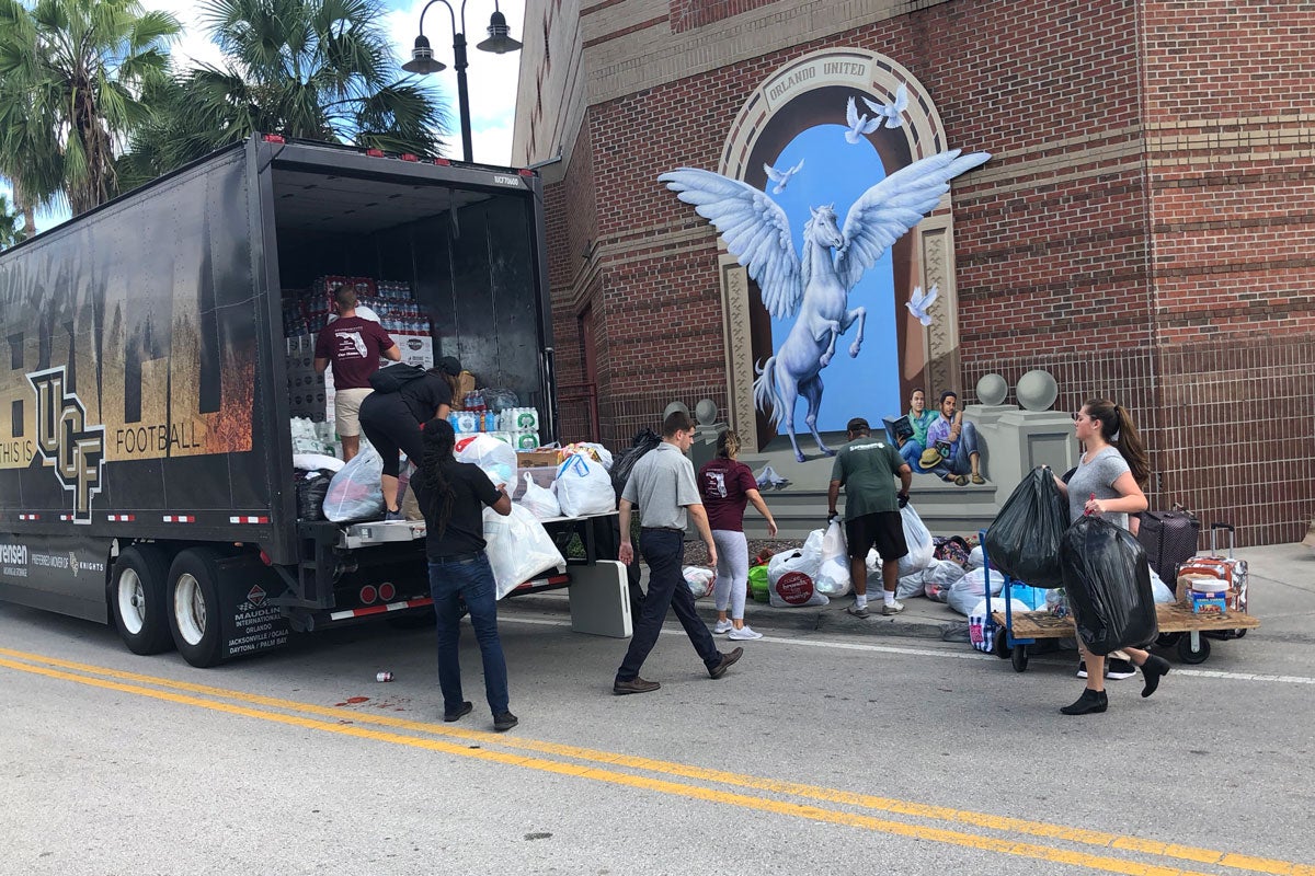 A group of people load bags of supplies into a moving truck outside of UCF's Student Union