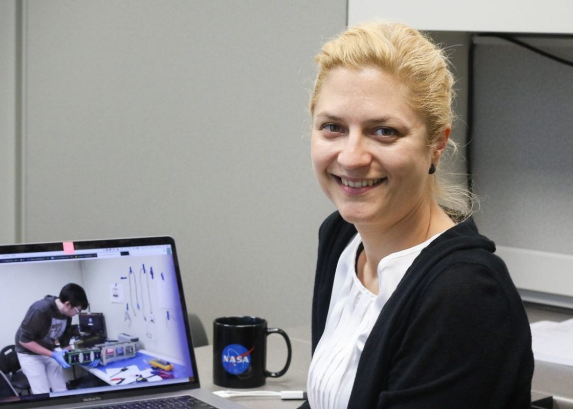 A blonde woman wearing a black sweater and white shirt sits at a computer