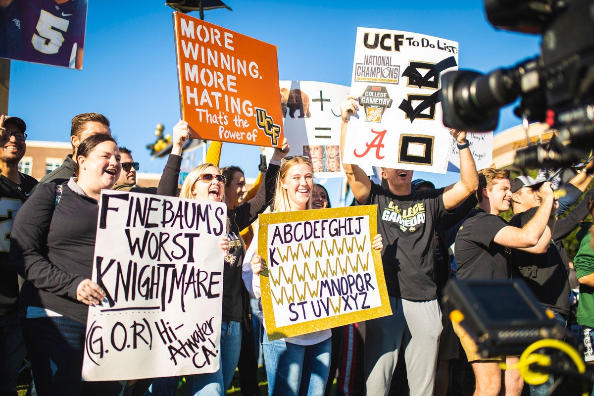 Fans holding up homemade signs about UCF Football in front of a camera lens