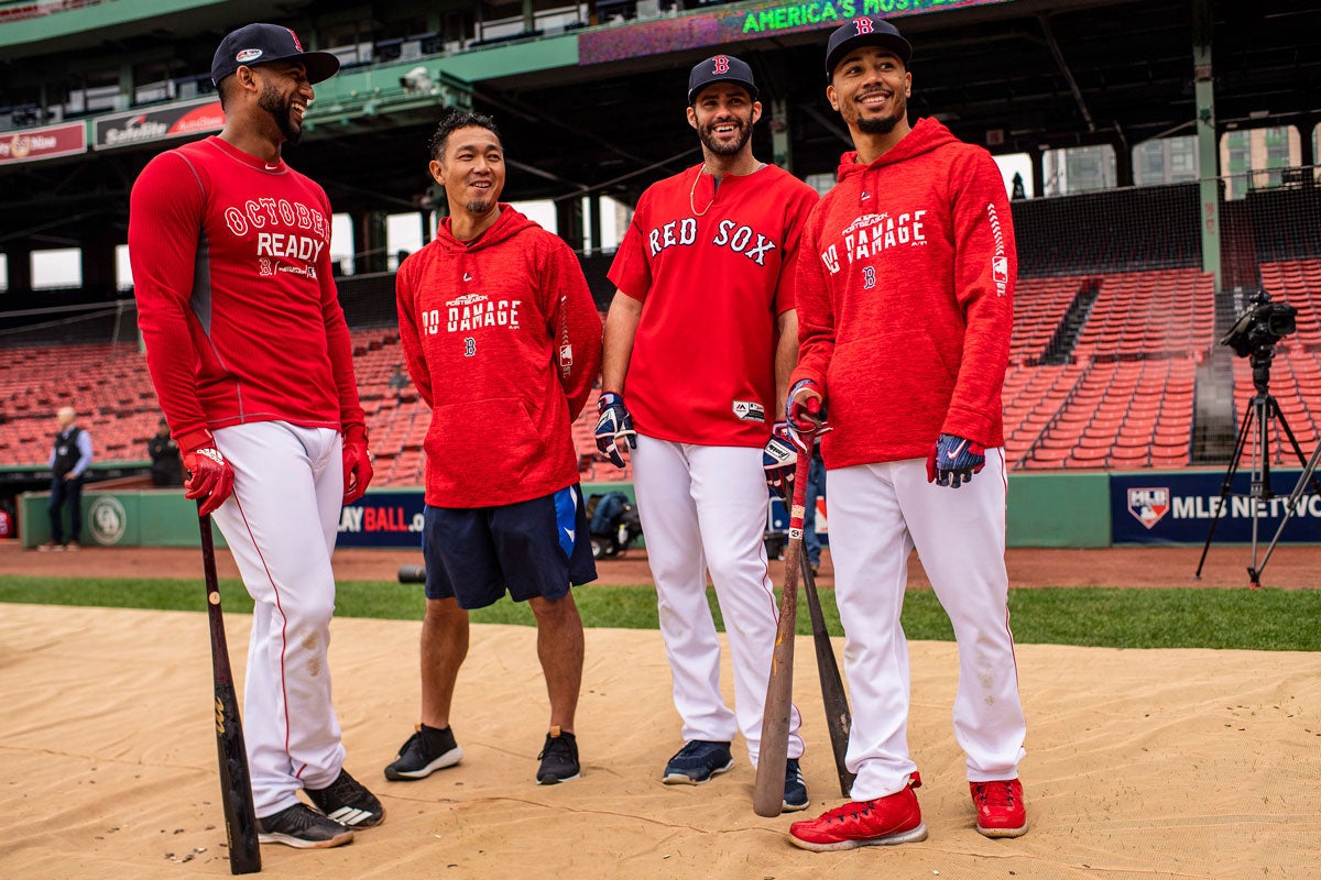 Four men in red Red Sox long sleeve shirts pose in Fenway Park