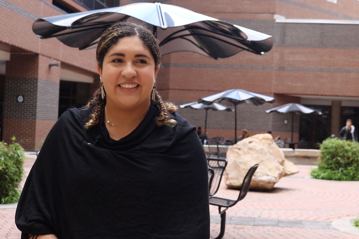 A woman wearing a black long sleeve shirt poses in front of a brick building