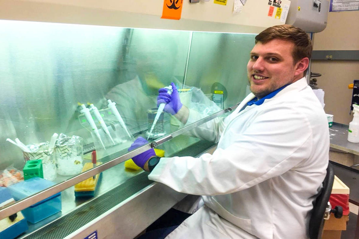 A man in a white lab coat holds a test tube