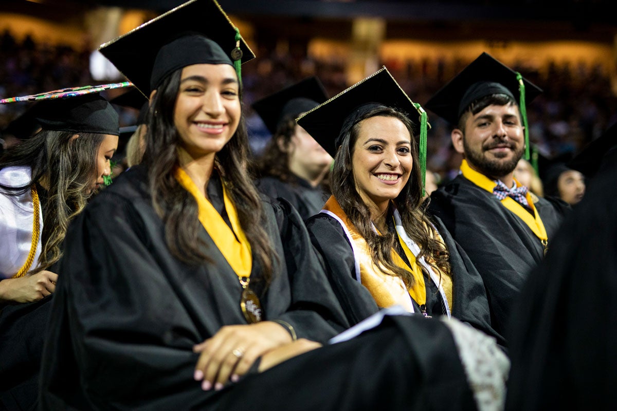 Two women and a man in caps and gowns smile at the camera.