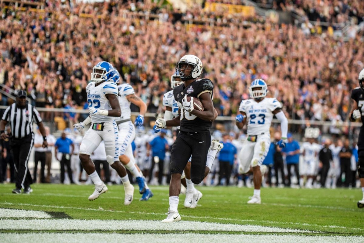 UCF player Greg McCrae wearing a white helmet and black uniform runs into end zone with Memphis defenders trailing him