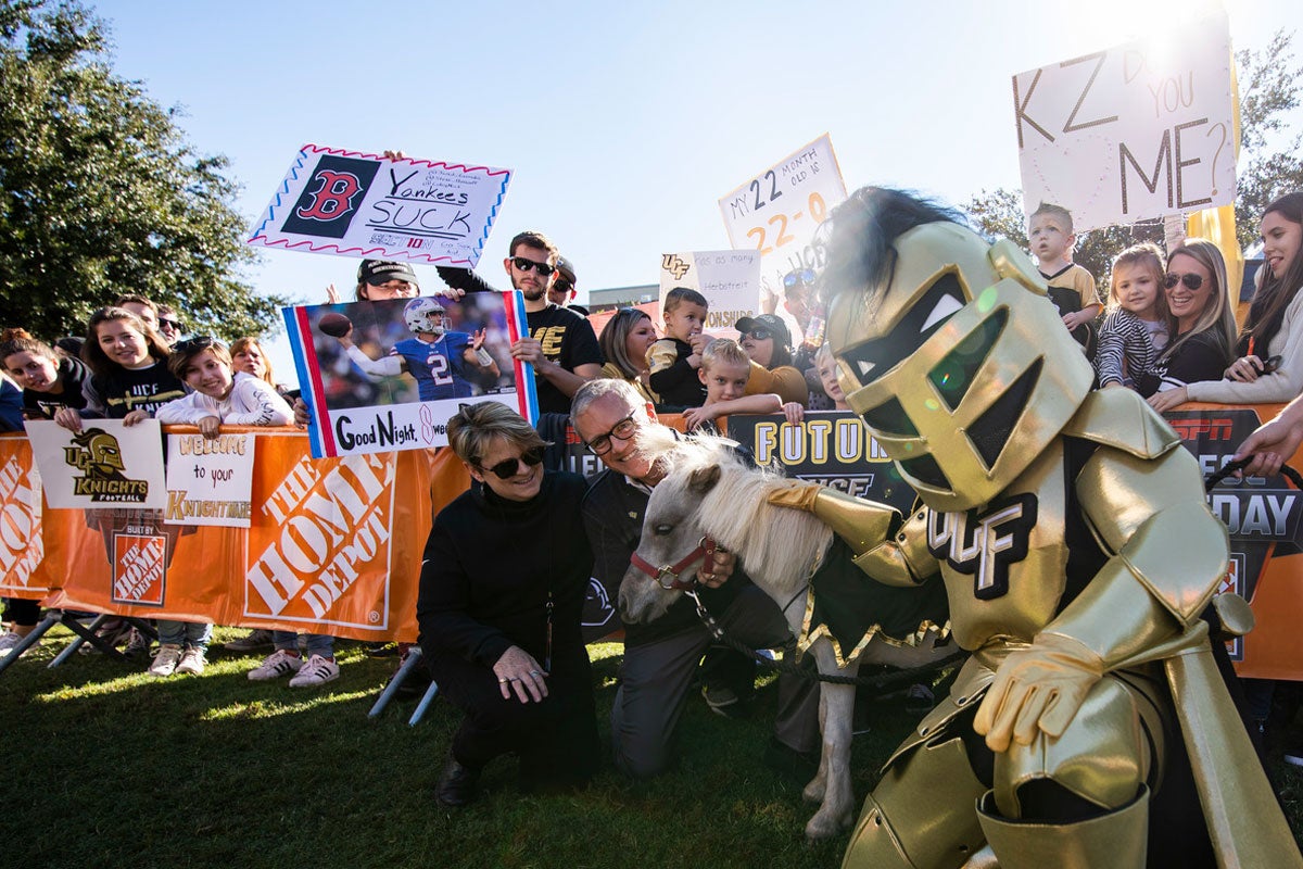 A man and woman kneel next to a mini horse with Knightro