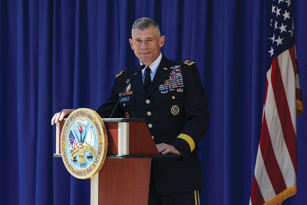 A man in a decorated Army uniform stands at a podium in front of a blue curtain