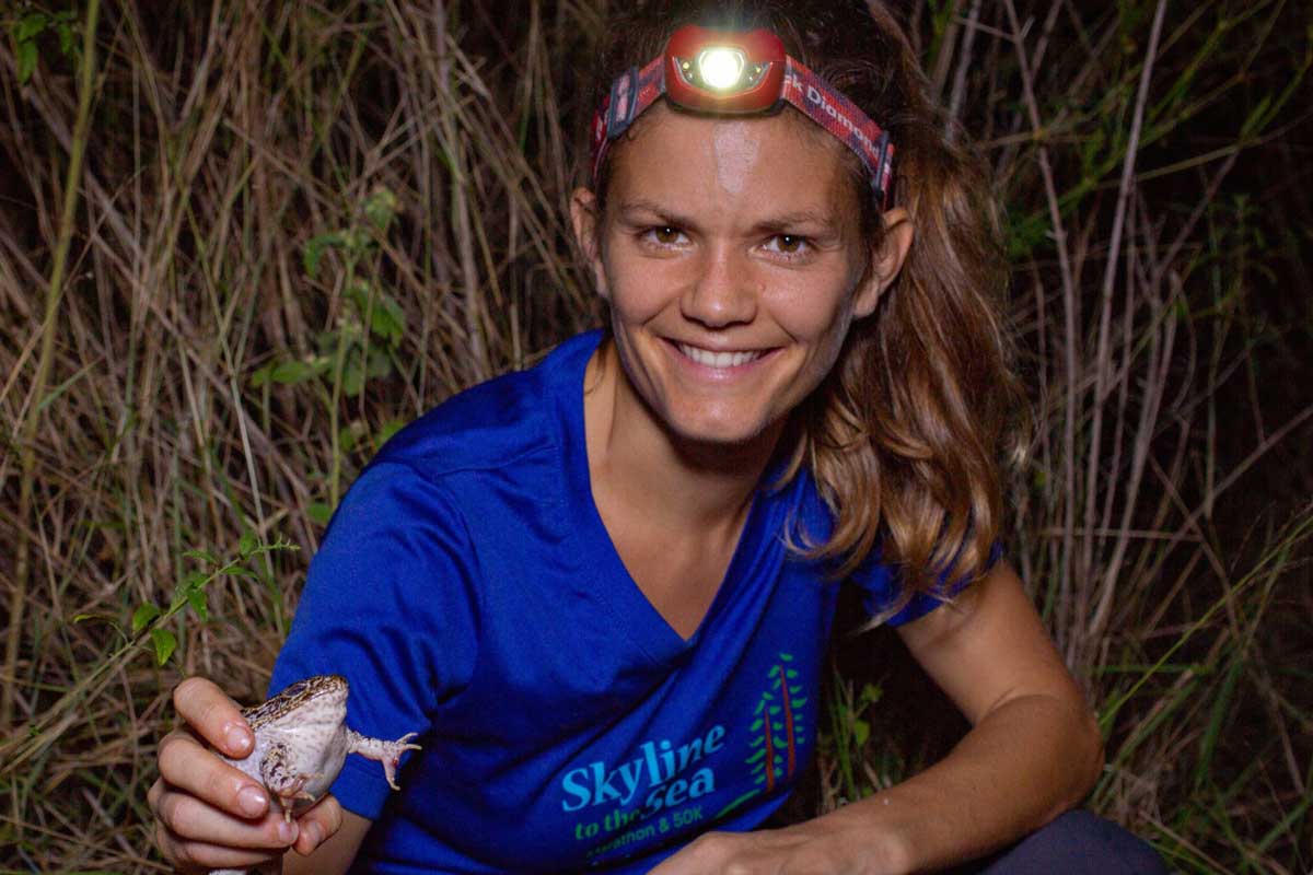 Blonde woman wearing head-flashlight and blue shirt holds a frog
