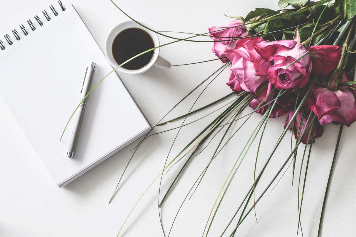 note pad, coffee and bouquet of pink roses on a table