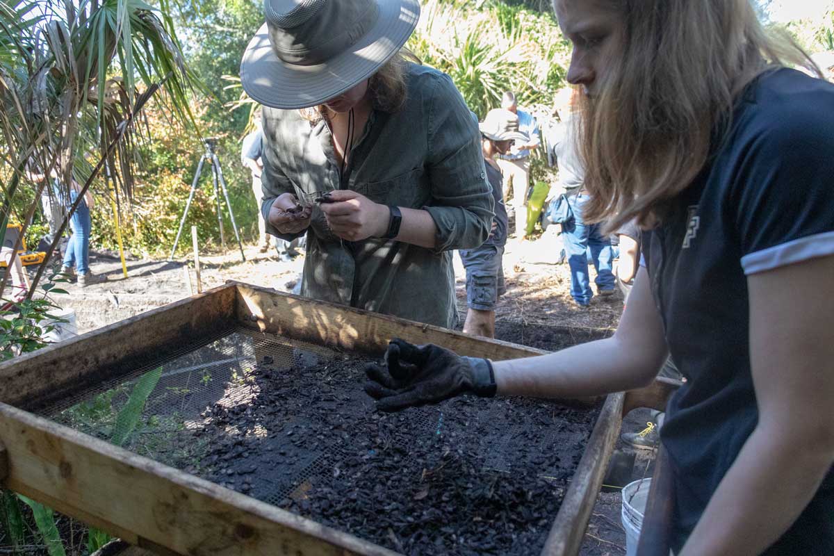 Two people use a wood box to sift through dirt