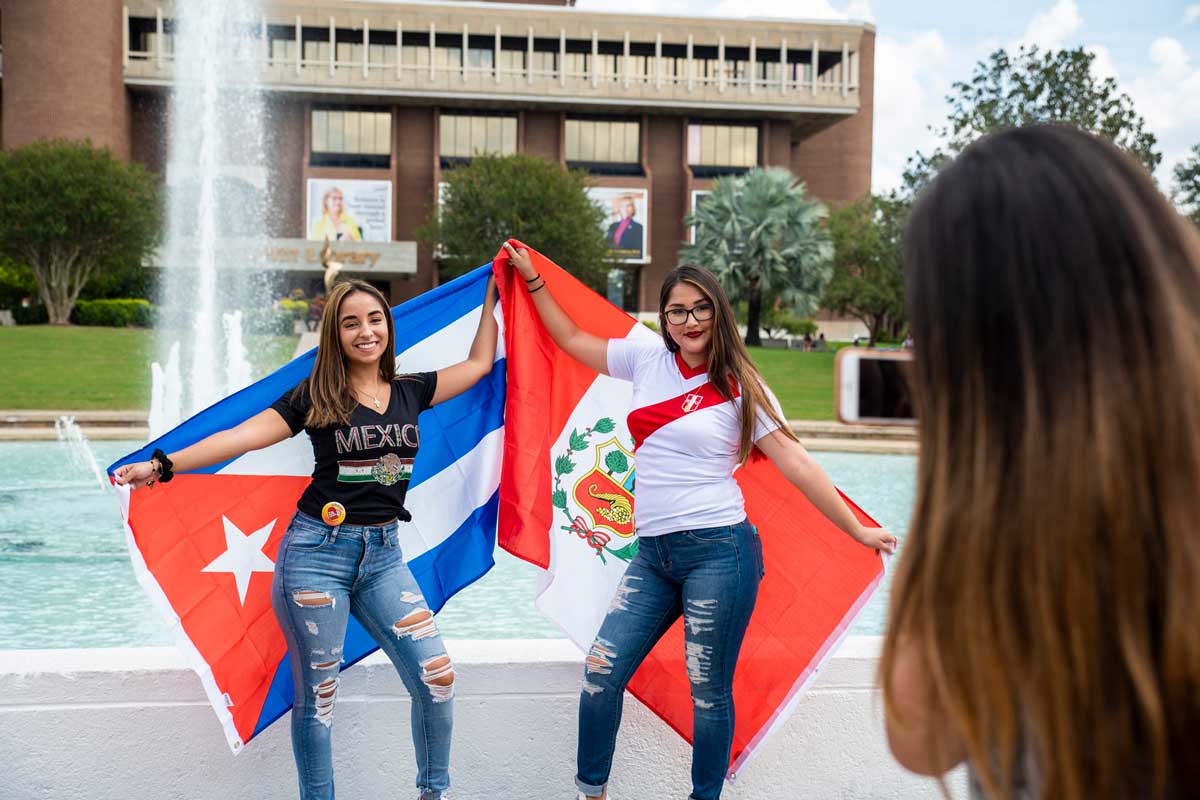 Two women pose with flags in front of fountain