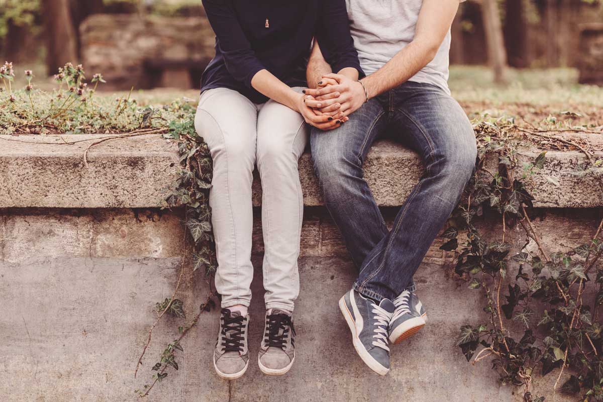 a couple holding hands while sitting on a ledge with their feet dangling
