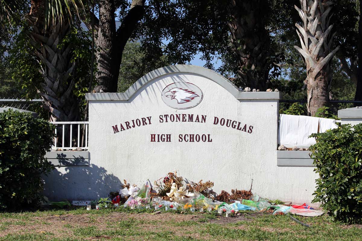 Concrete Marjory Stoneman Douglas High School sign with flowers piled in front of it