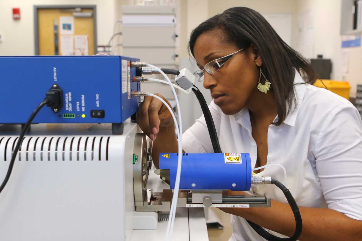 Woman in a lab studies a blue and gray machine with wires