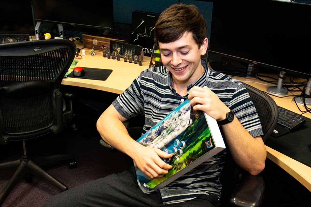 Brunette man sits at a desk and holds a painted keyboard