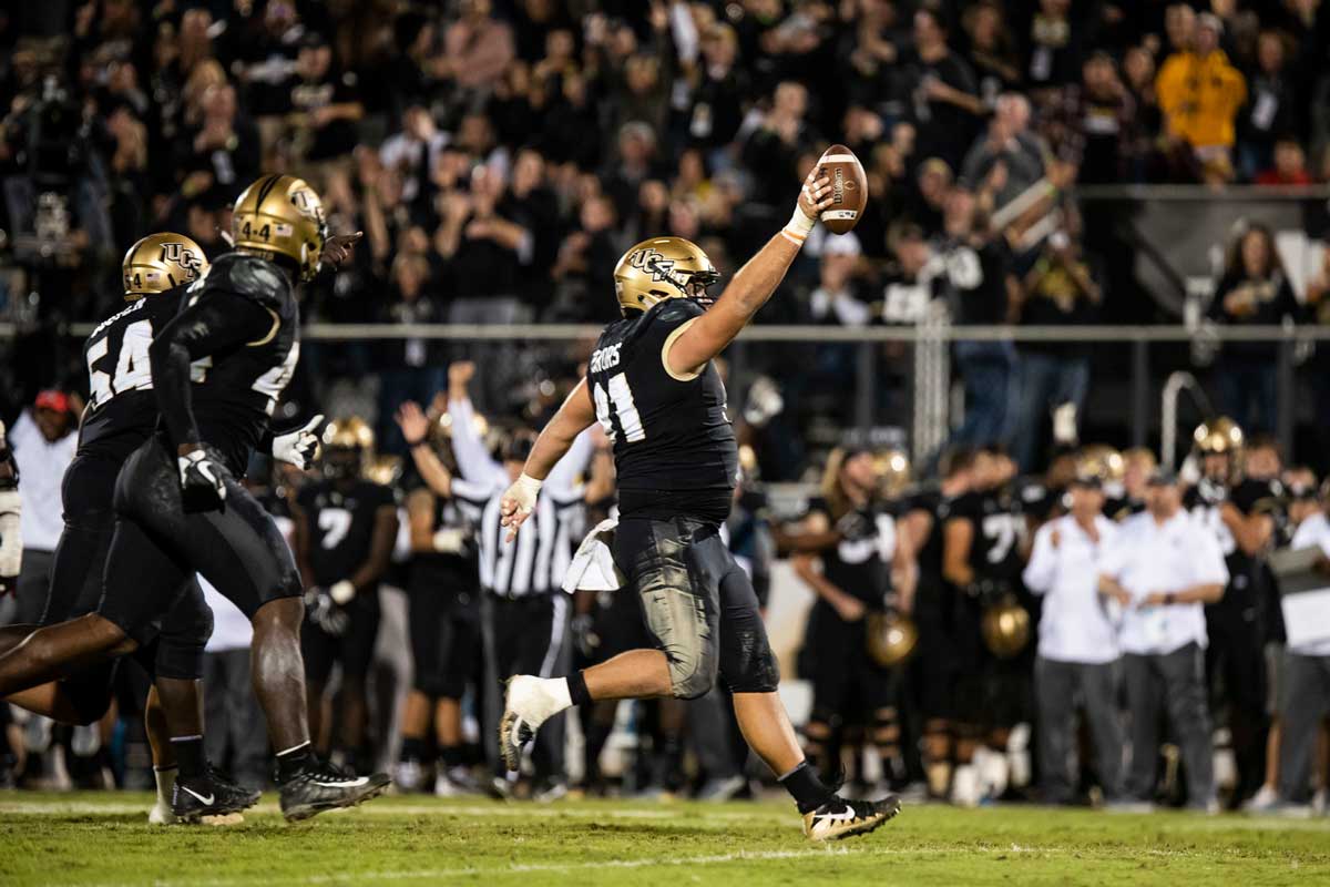 football player runs while holding up football with right hand