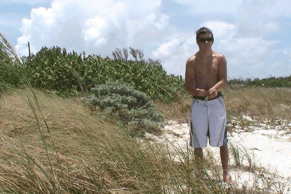 Young man wearing sunglasses and bathing suit standing next to sand dunes
