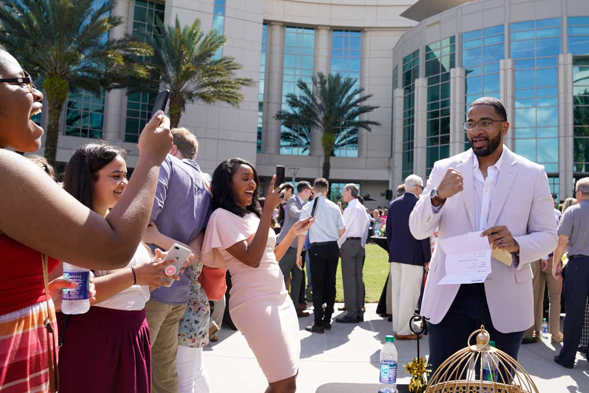 Man fist pumps with three women taking photos on cell phones